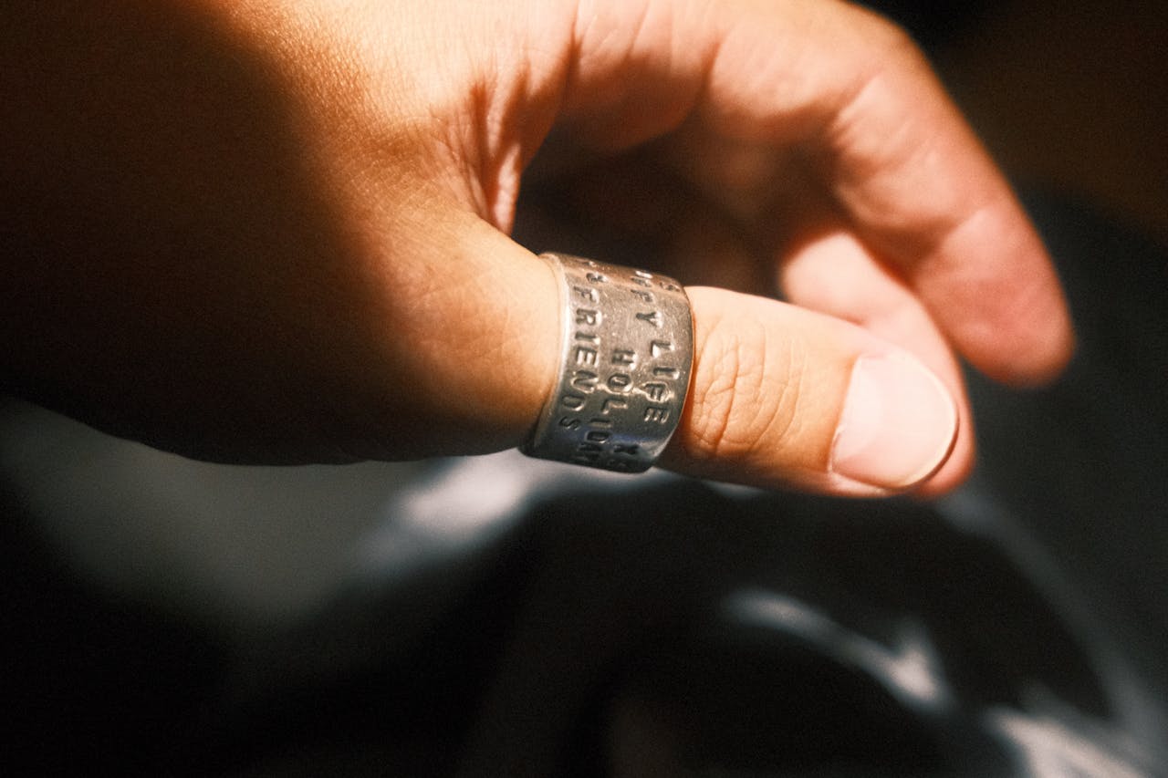 A close-up of a hand wearing an inscribed silver ring, captured in warm sunlight.